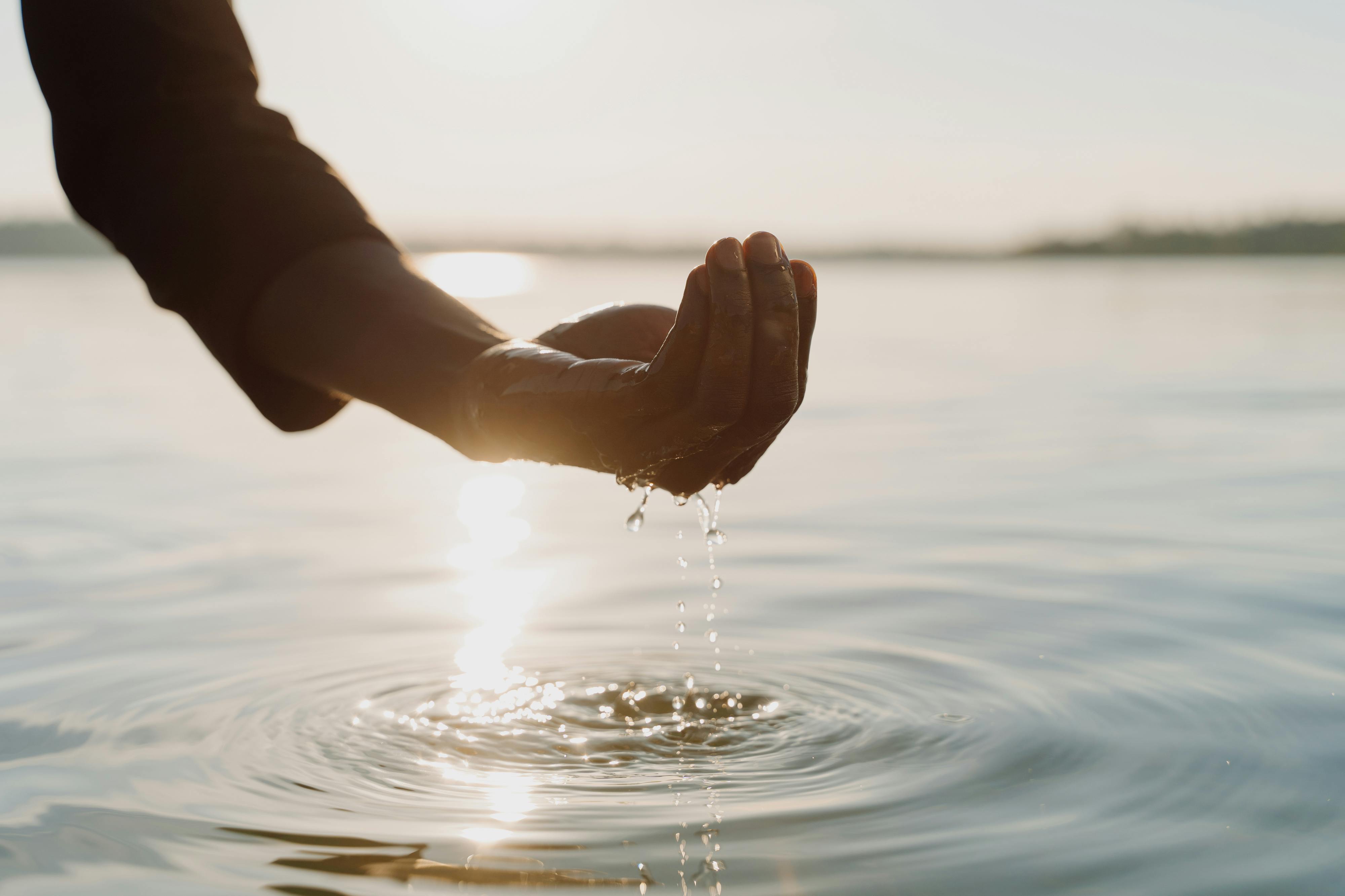 Close-up of a hand holding water with sunlight reflecting on the water surface.