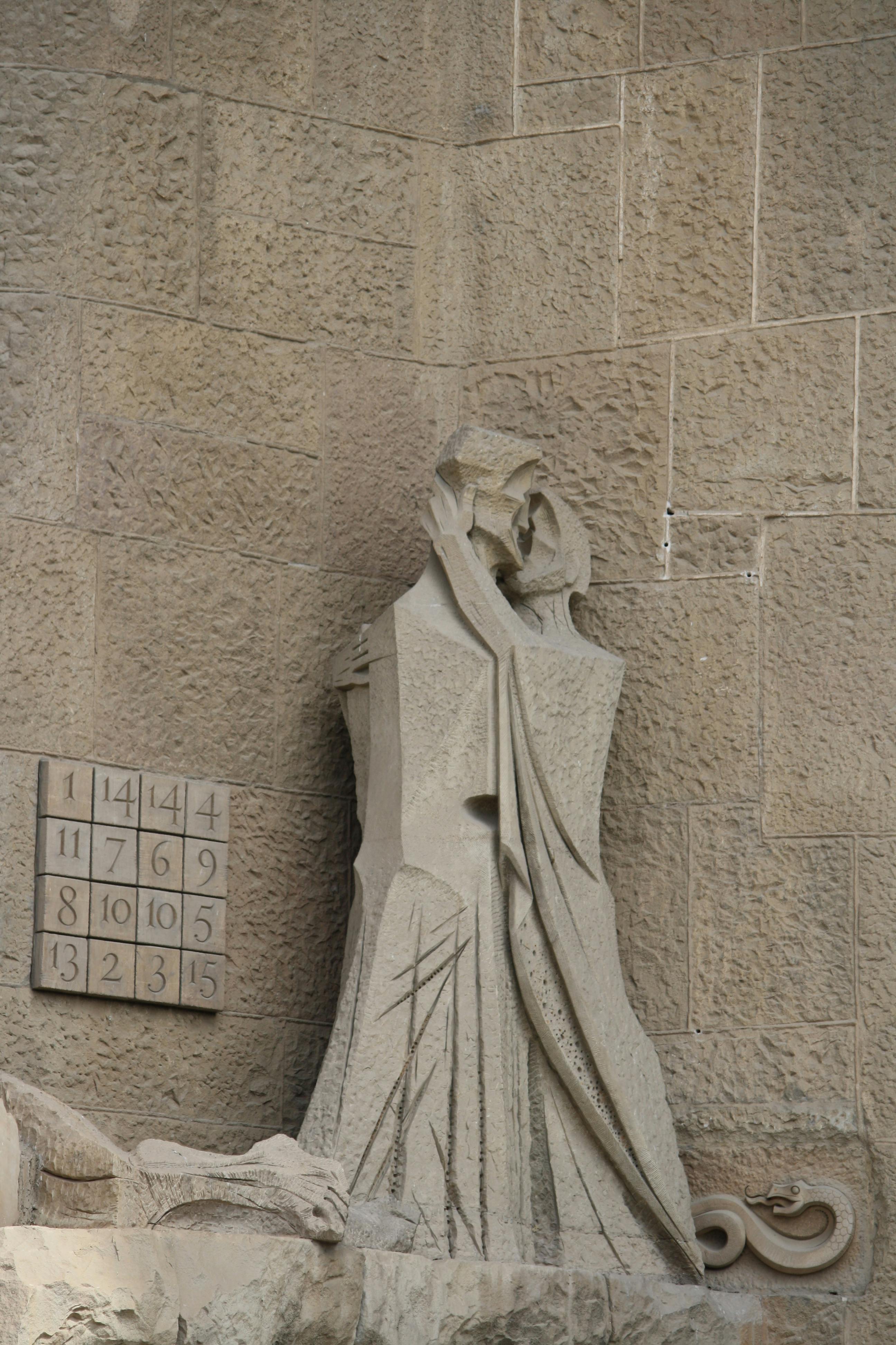 Stone sculpture of a couple in an artistic embrace against a textured wall with a numeric board.