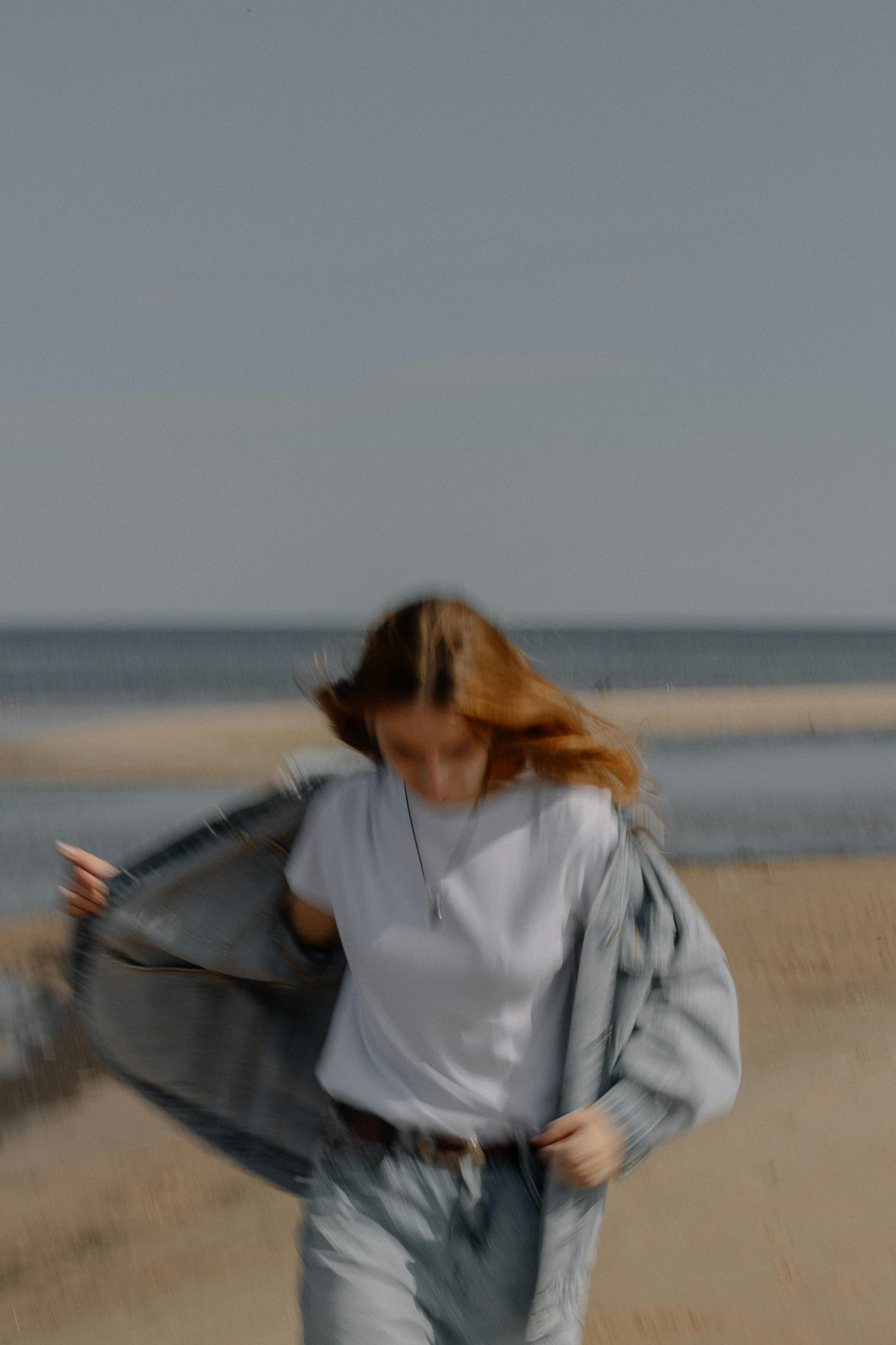 A woman in casual attire walking along a blurry sandy beach under a sunny sky.