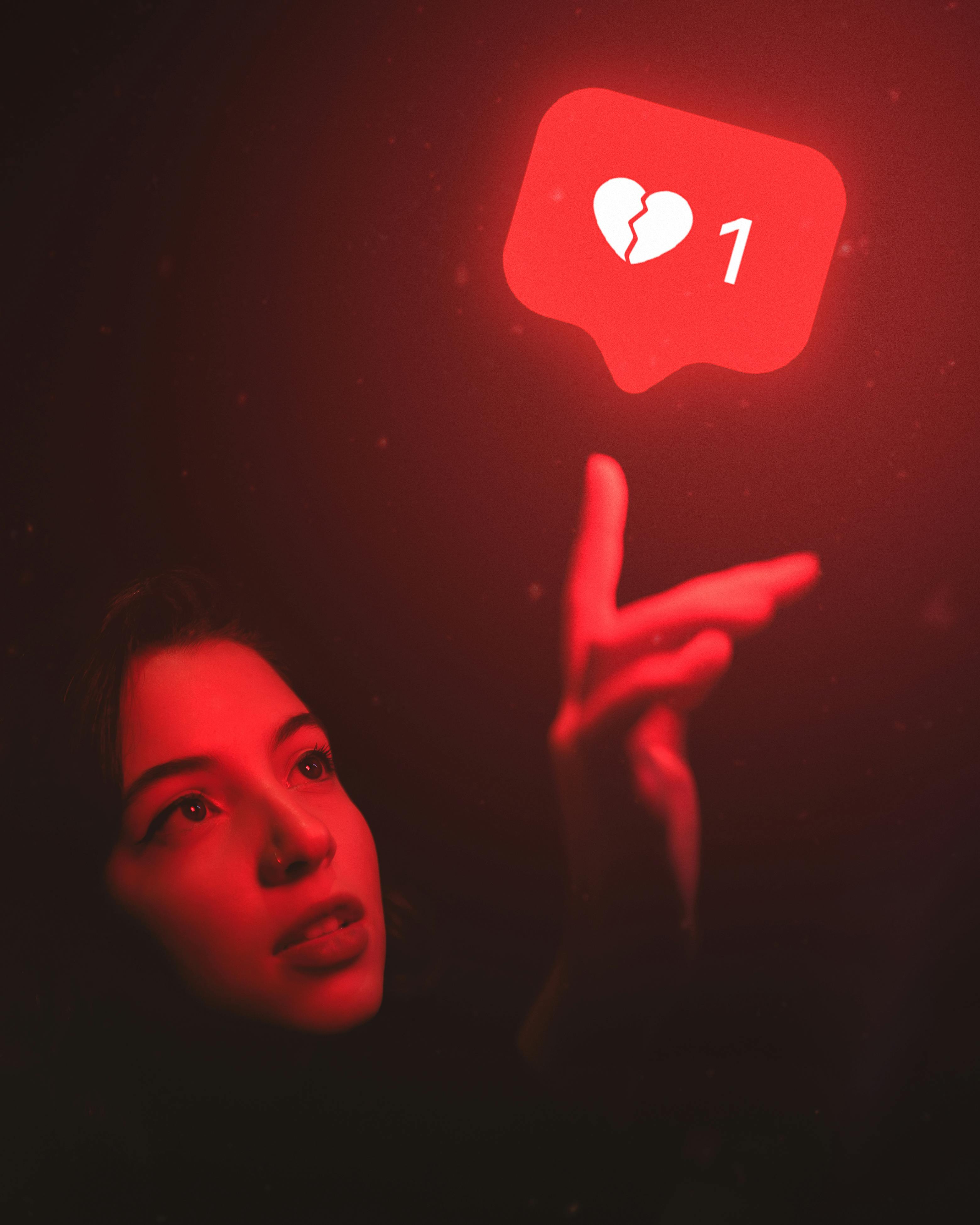 Red-hued image of a woman reaching towards a broken heart icon symbolizing digital detachment.