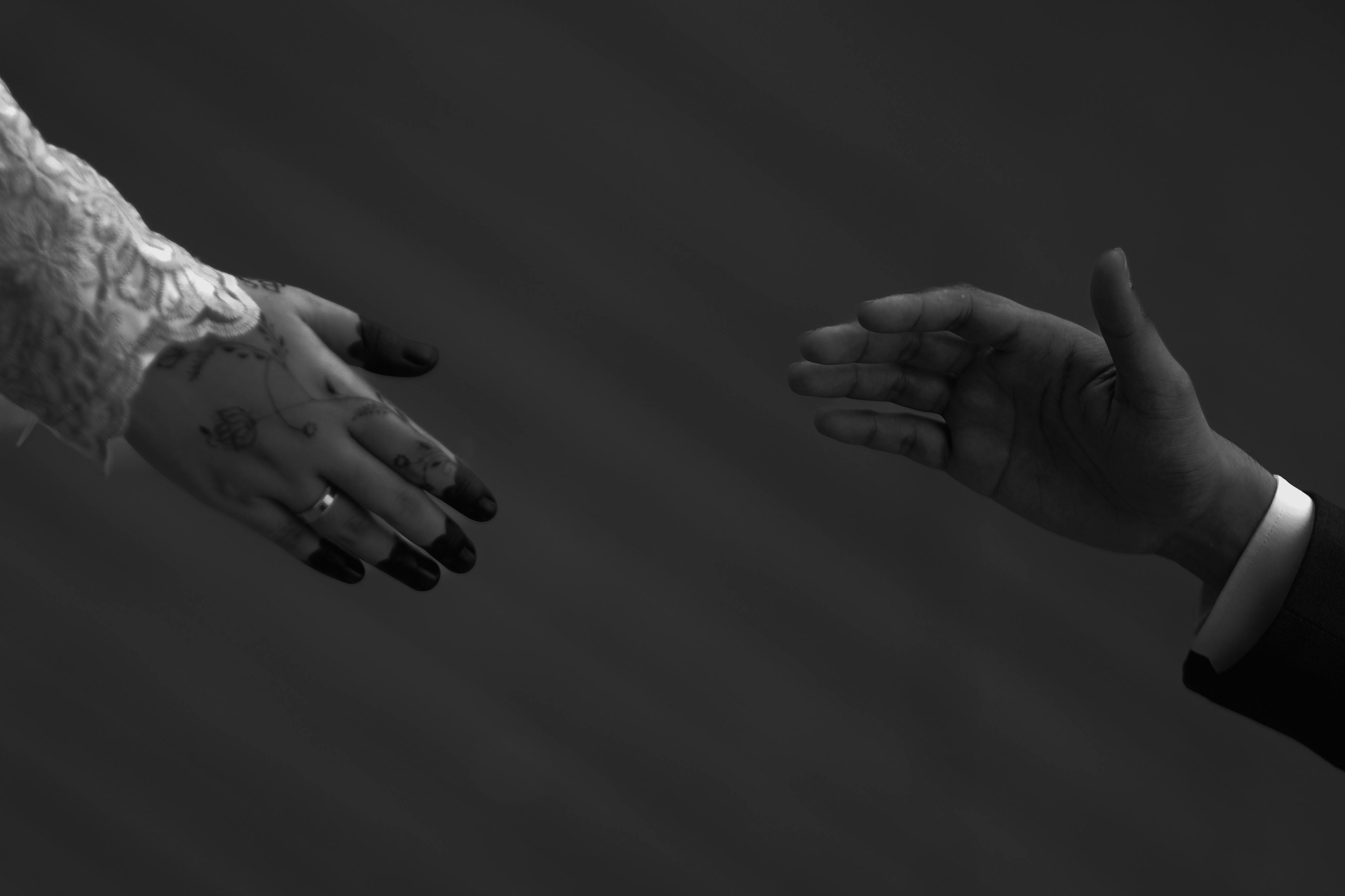 A black and white image of two hands reaching for each other, symbolizing connection.