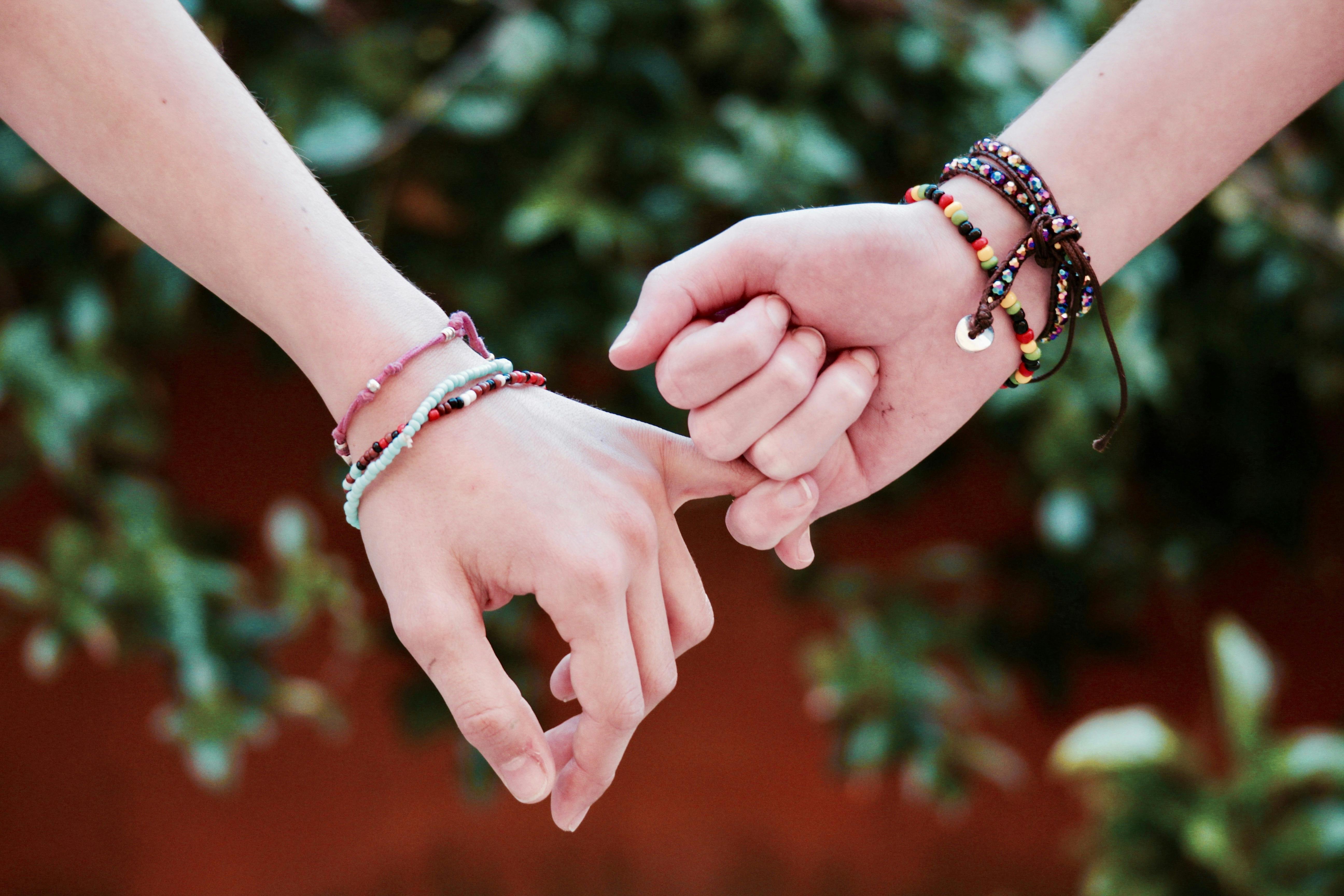 Two hands with colorful bracelets interlocked, symbolizing friendship and connection.