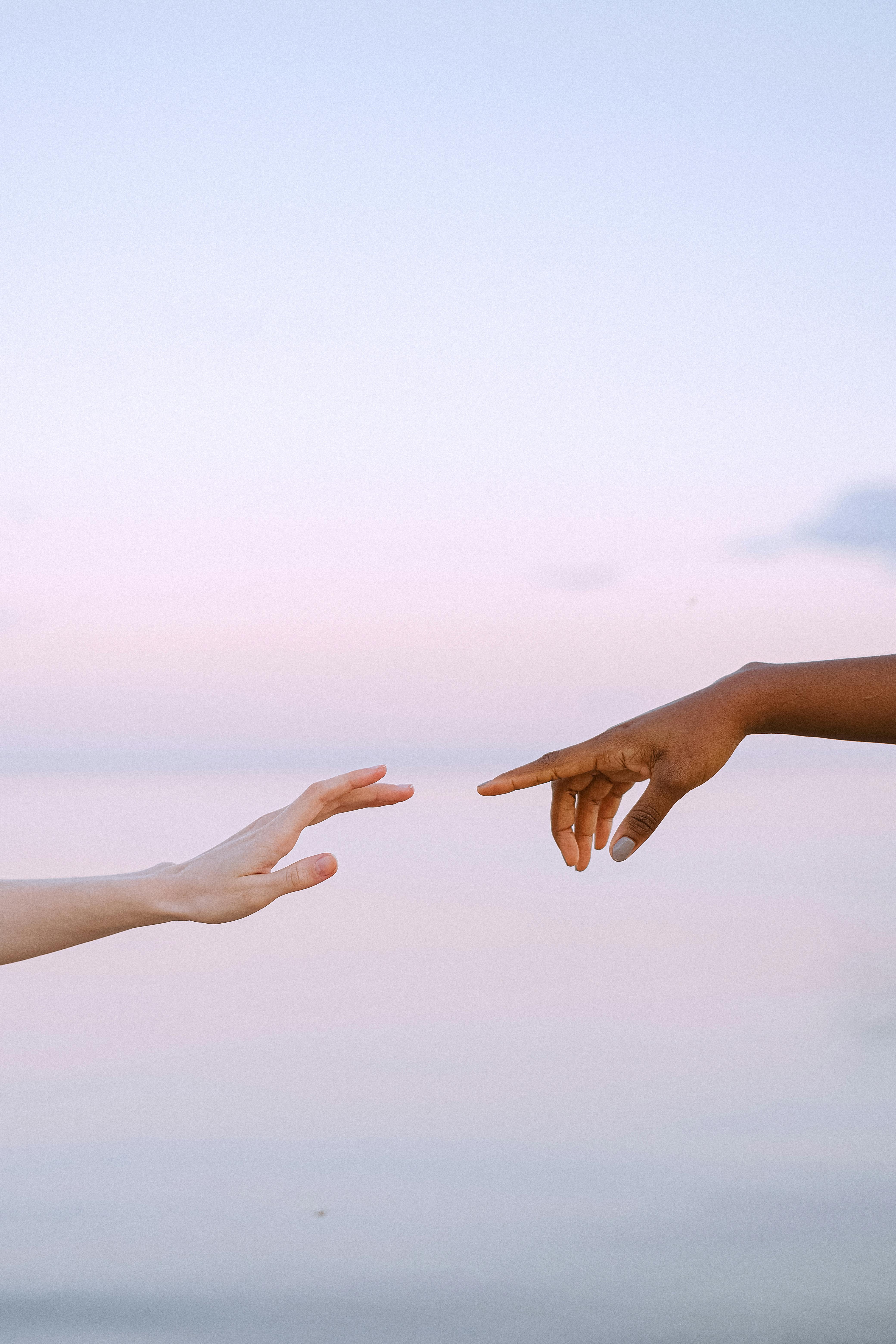 Two diverse hands reaching towards each other over a serene pastel sky and water background.