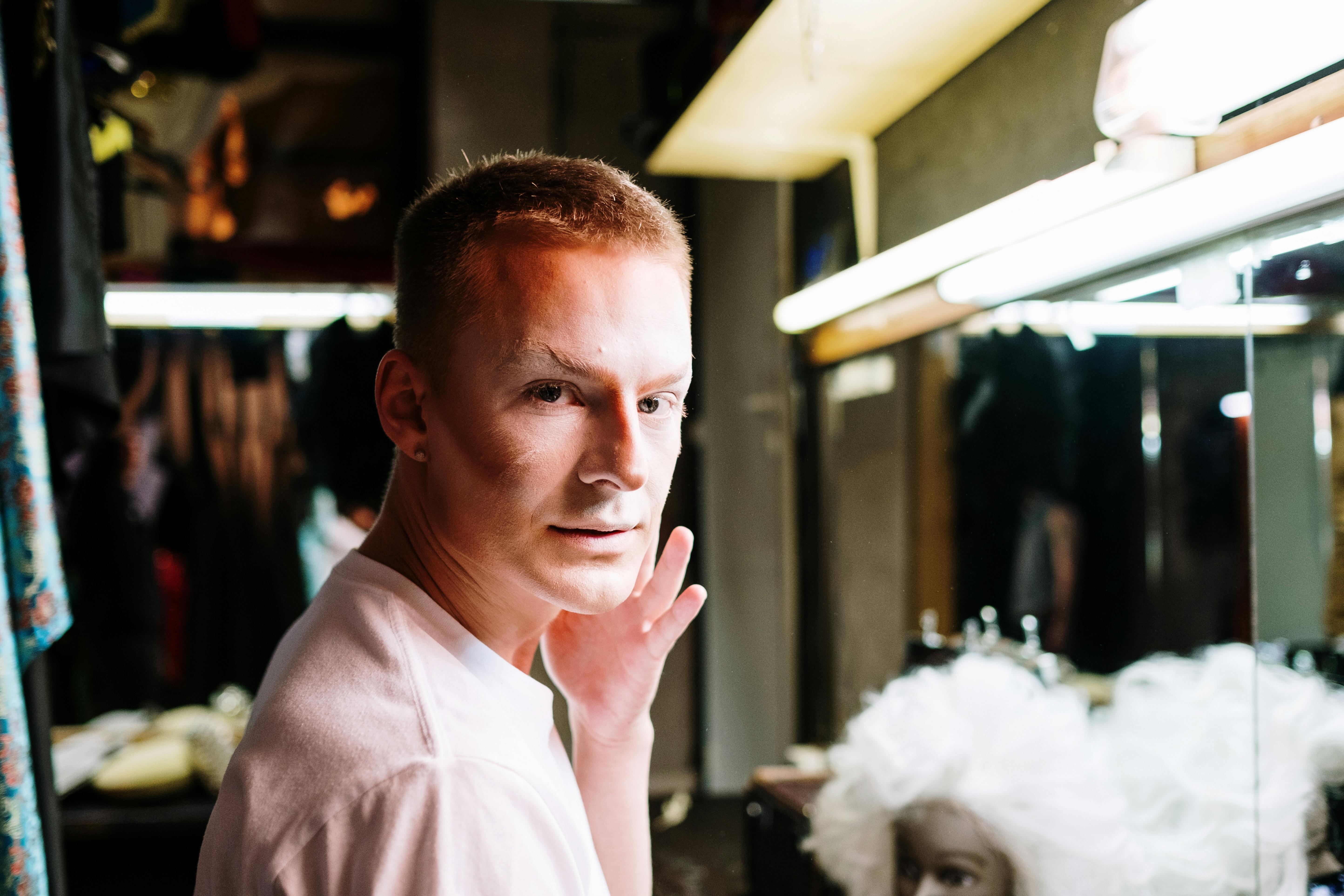 A drag performer applying makeup in a dressing room, highlighting identity and transformation.