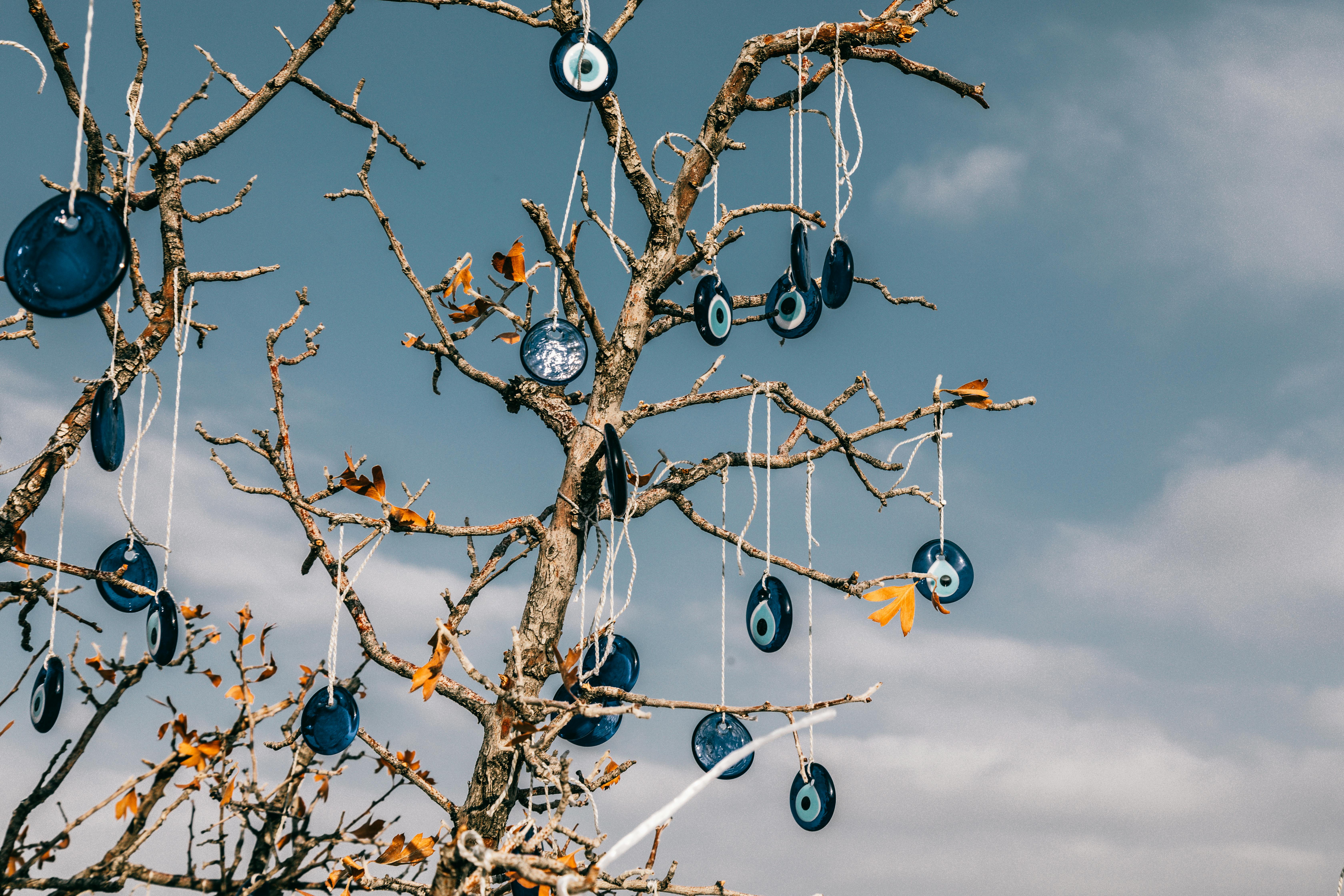 From below of traditional blue eye shaped nazar amulets protecting form evil eye hanging on leafless tree branches against cloudy blue sky in Cappadocia