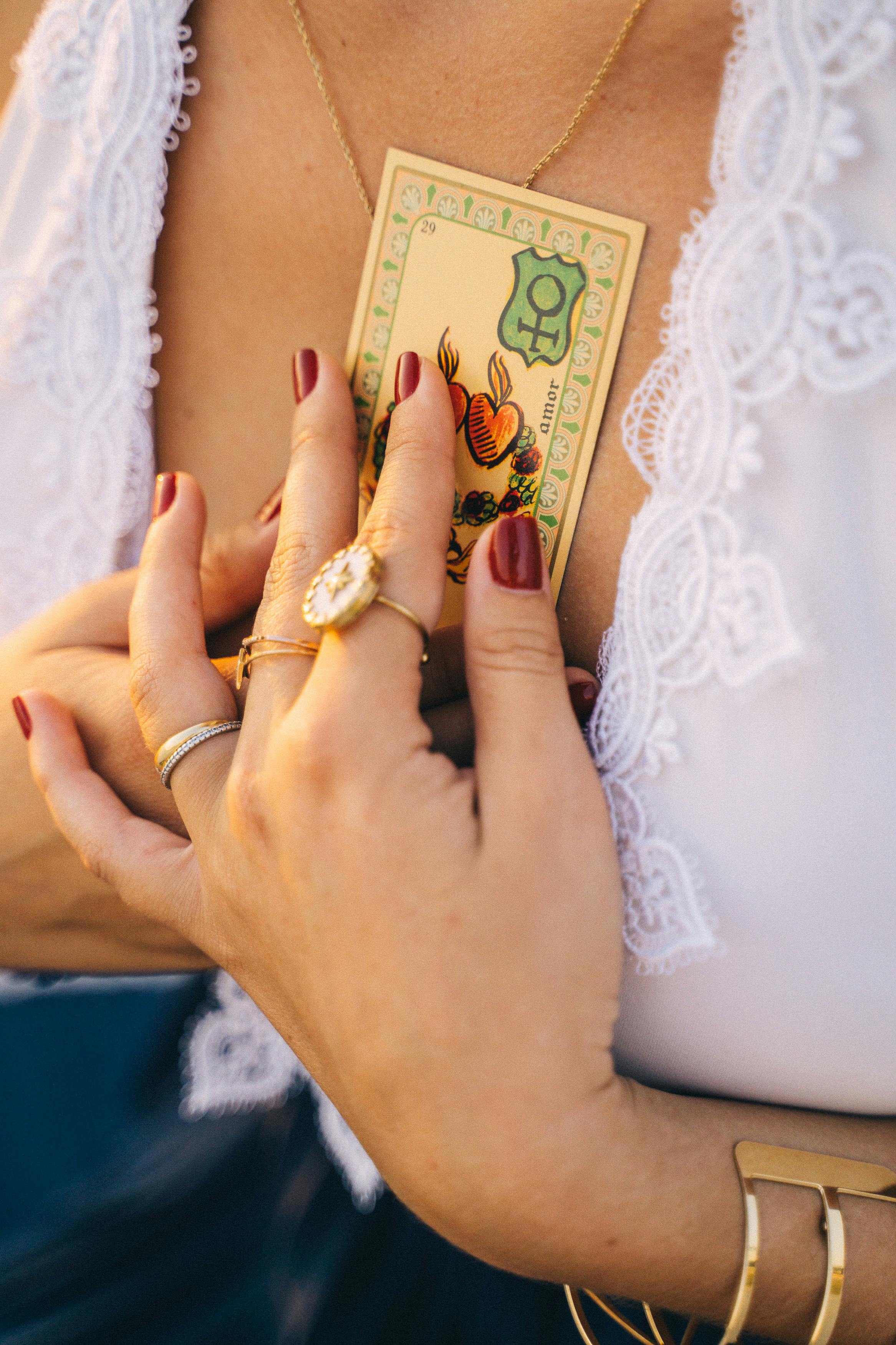 Close-up of woman holding tarot card to her chest with jewelry on hands.