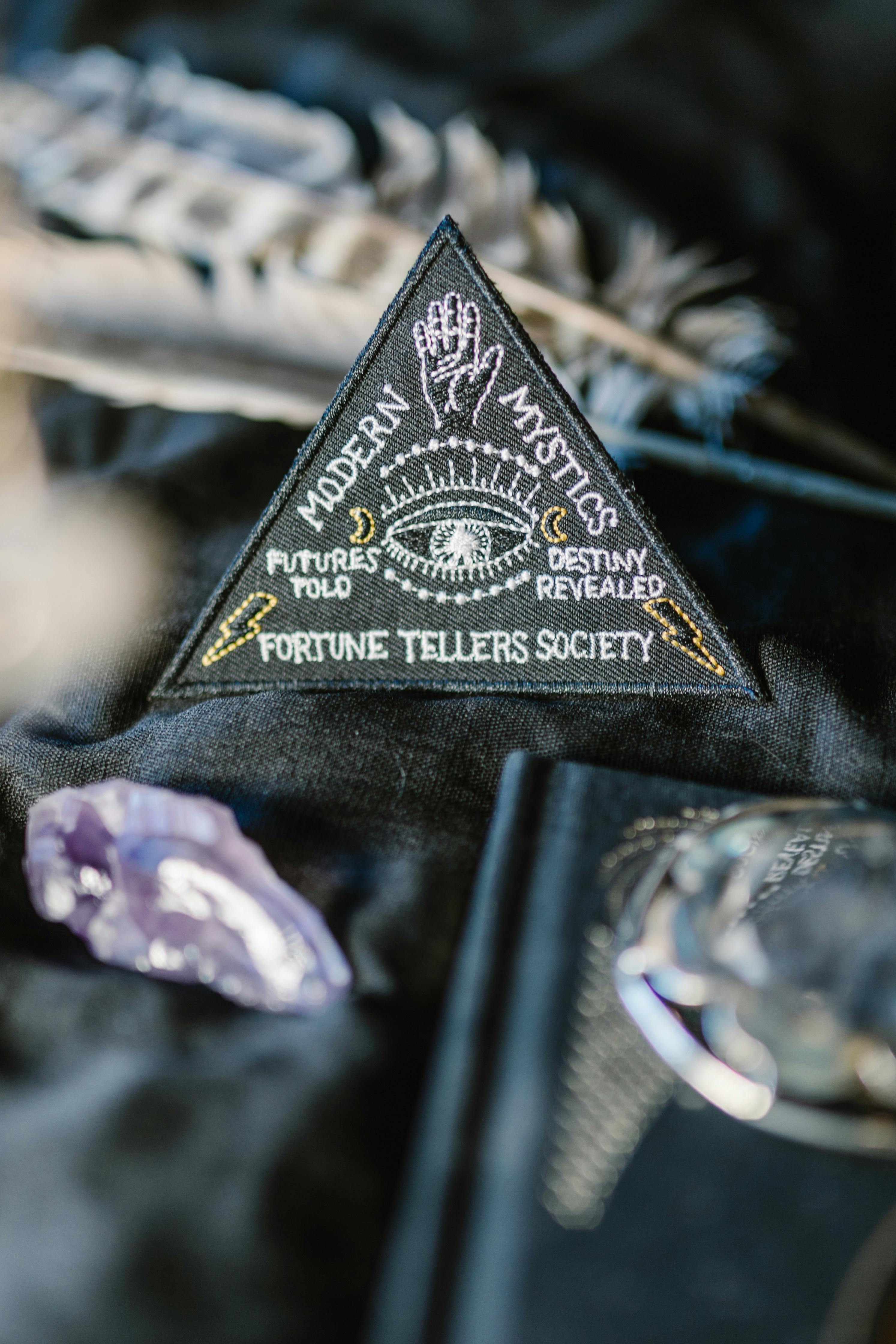 A mystical triangle patch with fortune-telling themes surrounded by crystals and feathers on dark background.