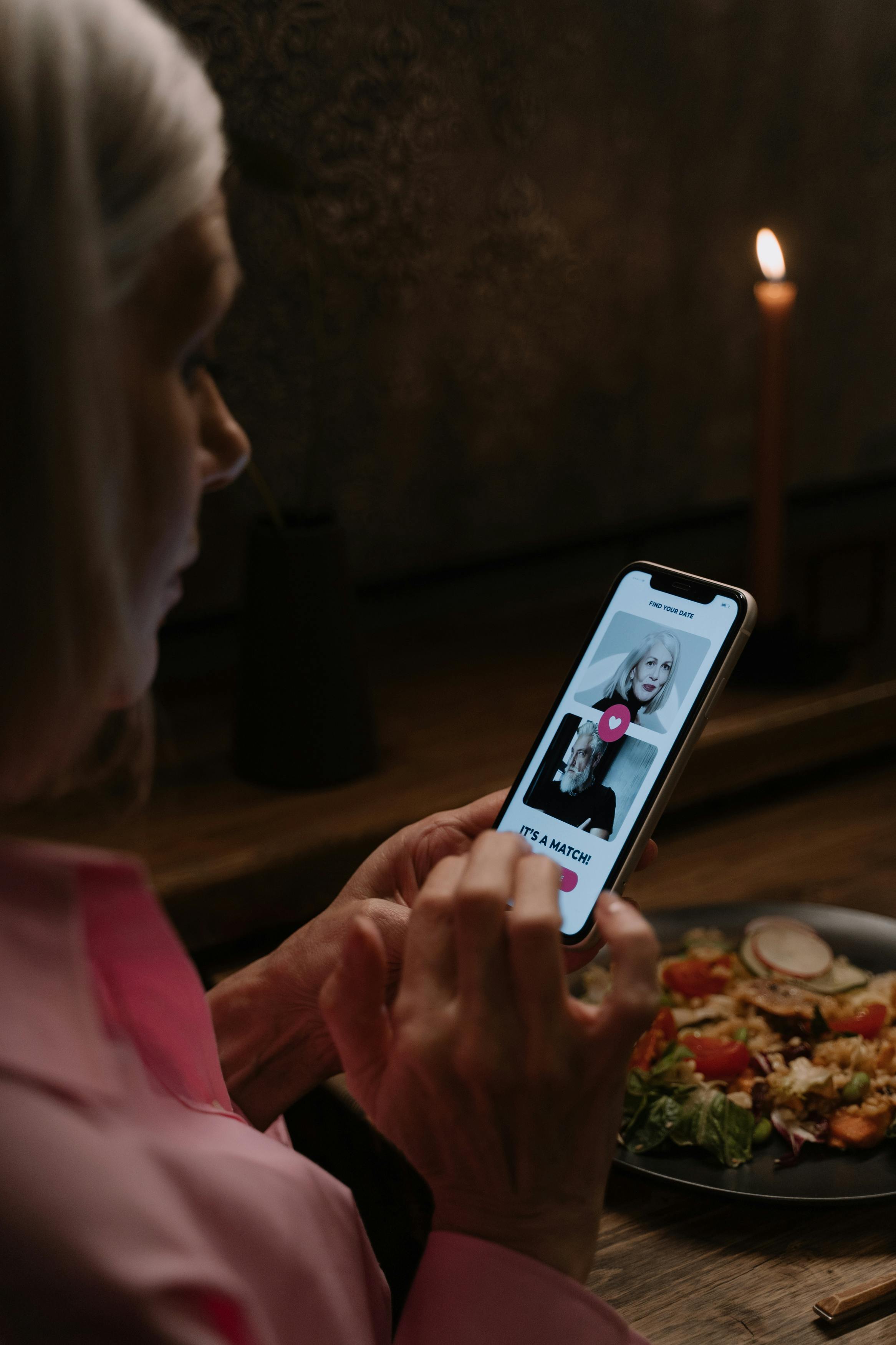 Elderly woman explores dating app during a cozy dinner.