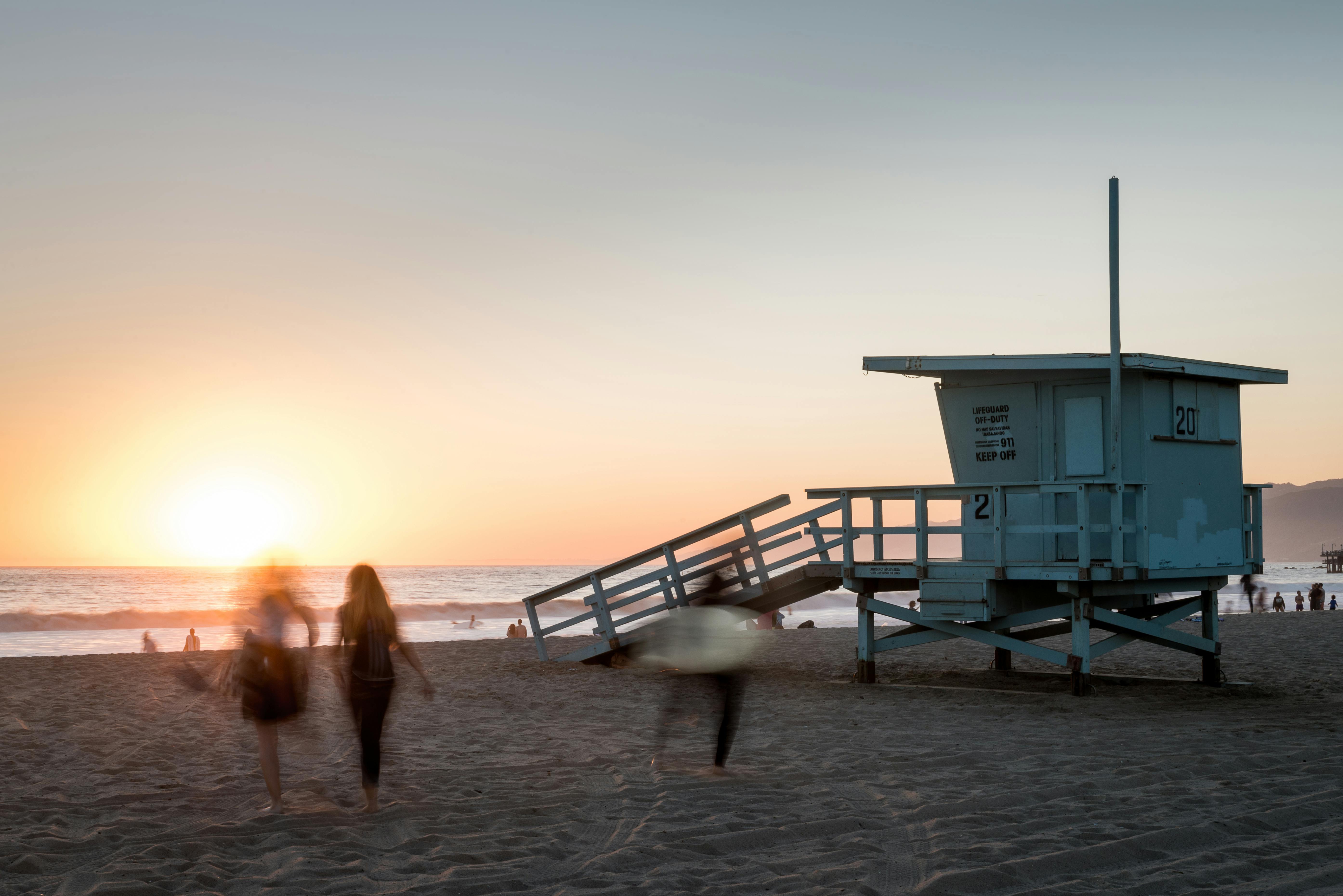 Beach scene at sunset with a lifeguard tower and people in motion at Santa Monica, CA.