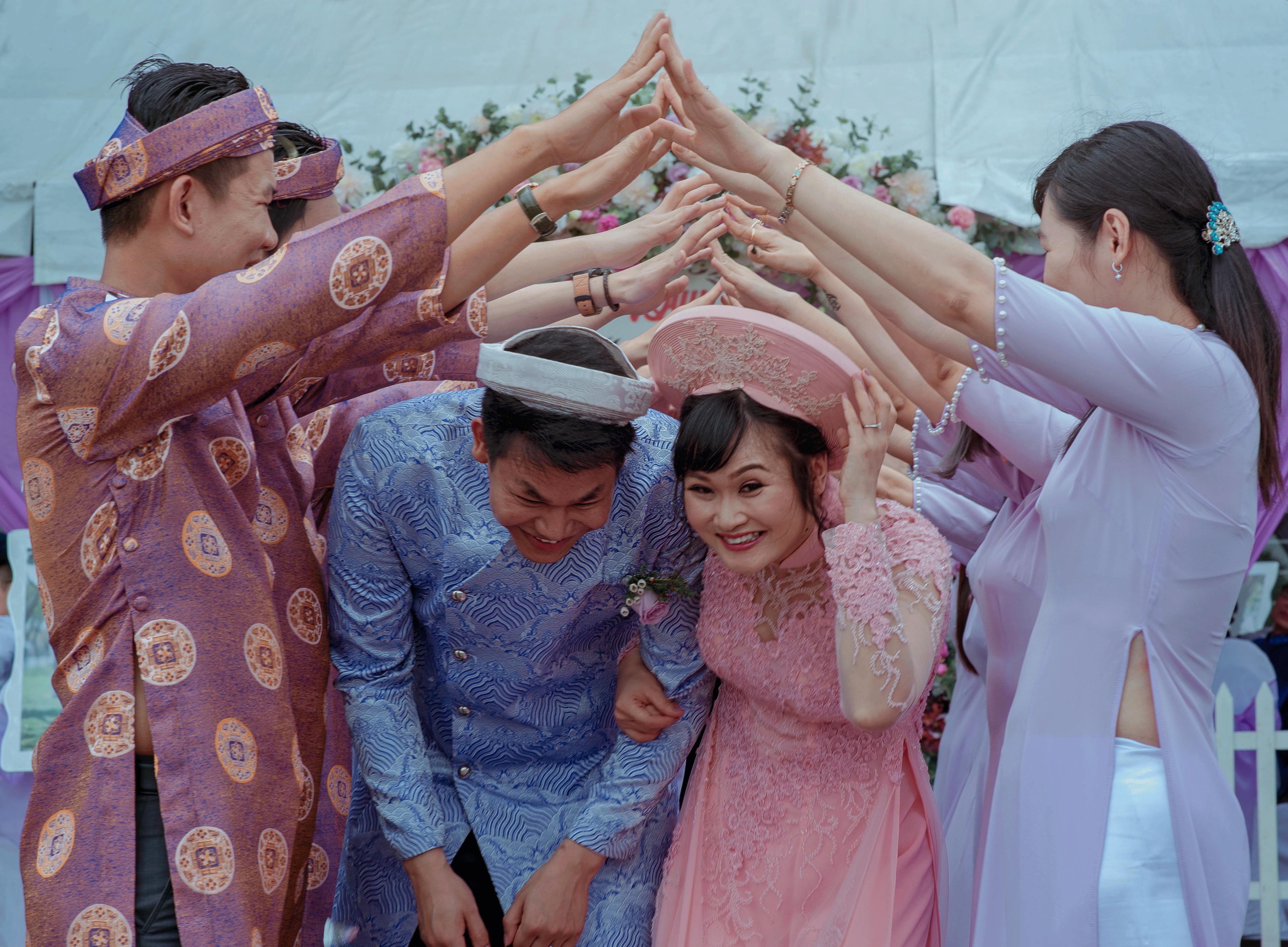 Happy Vietnamese couple celebrates their wedding with friends in traditional attire outdoors.