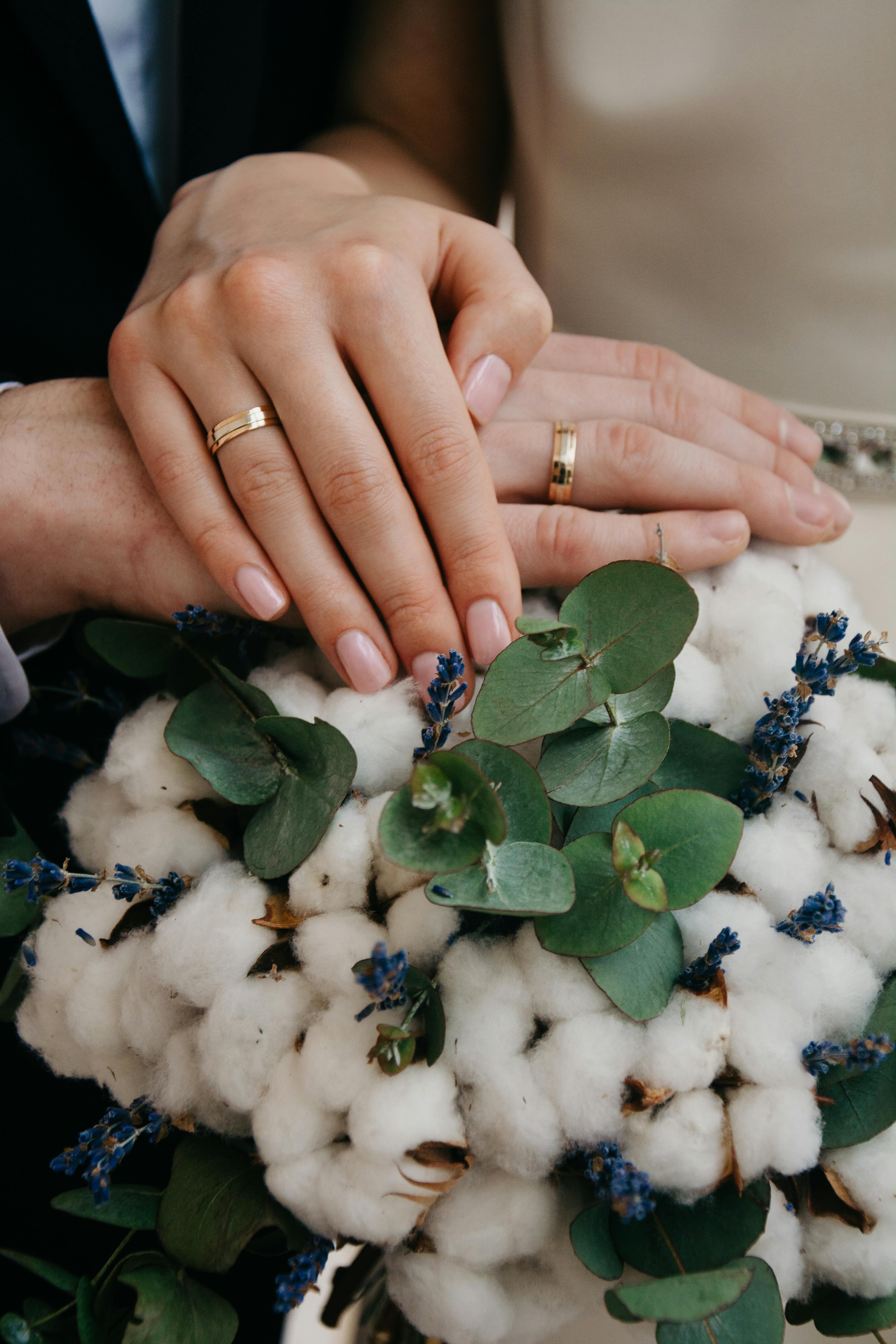 Close-up of couple's hands with gold wedding bands over a floral bouquet.