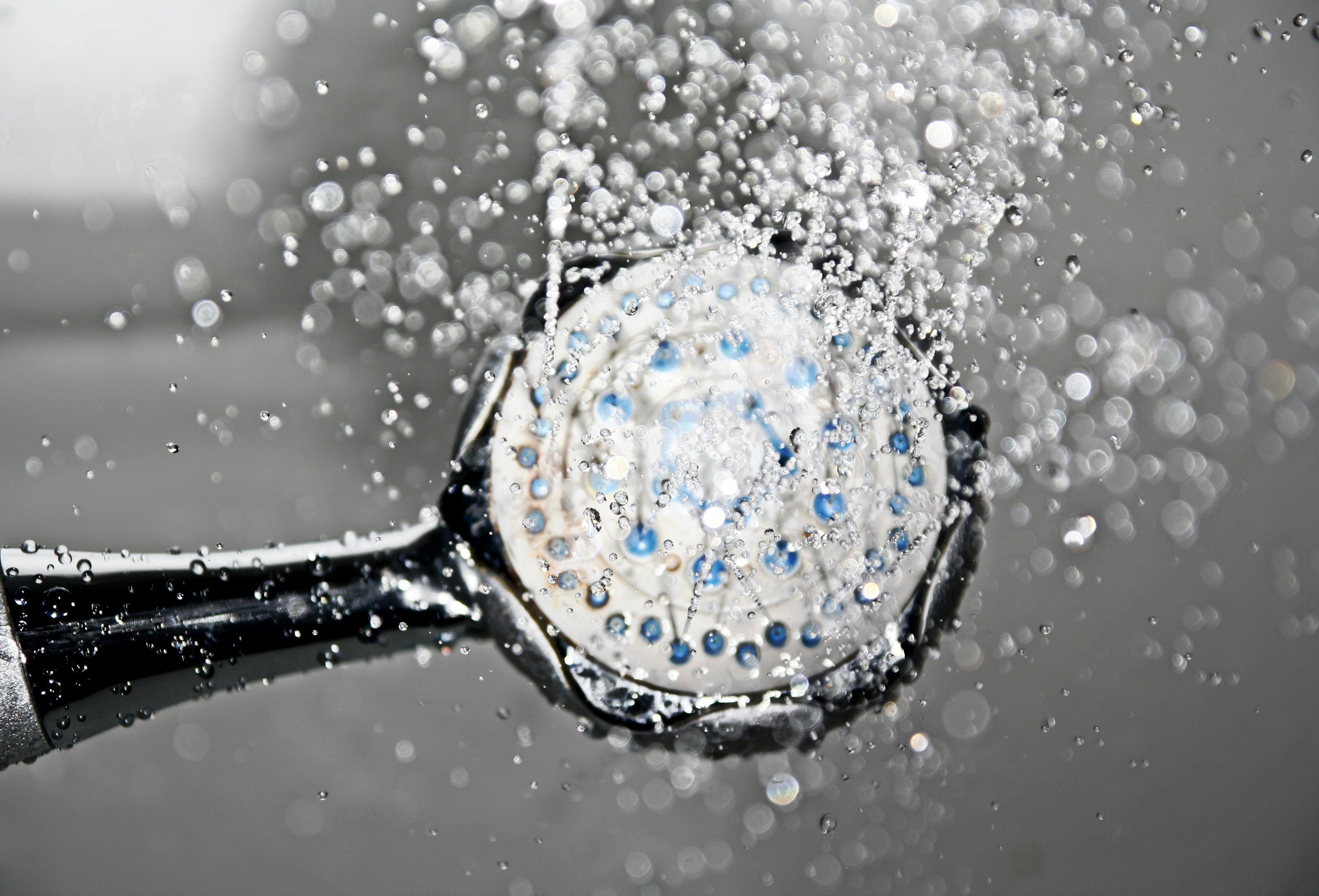 Close-up of a shower head releasing water droplets, creating a crisp and refreshing bathroom scene.