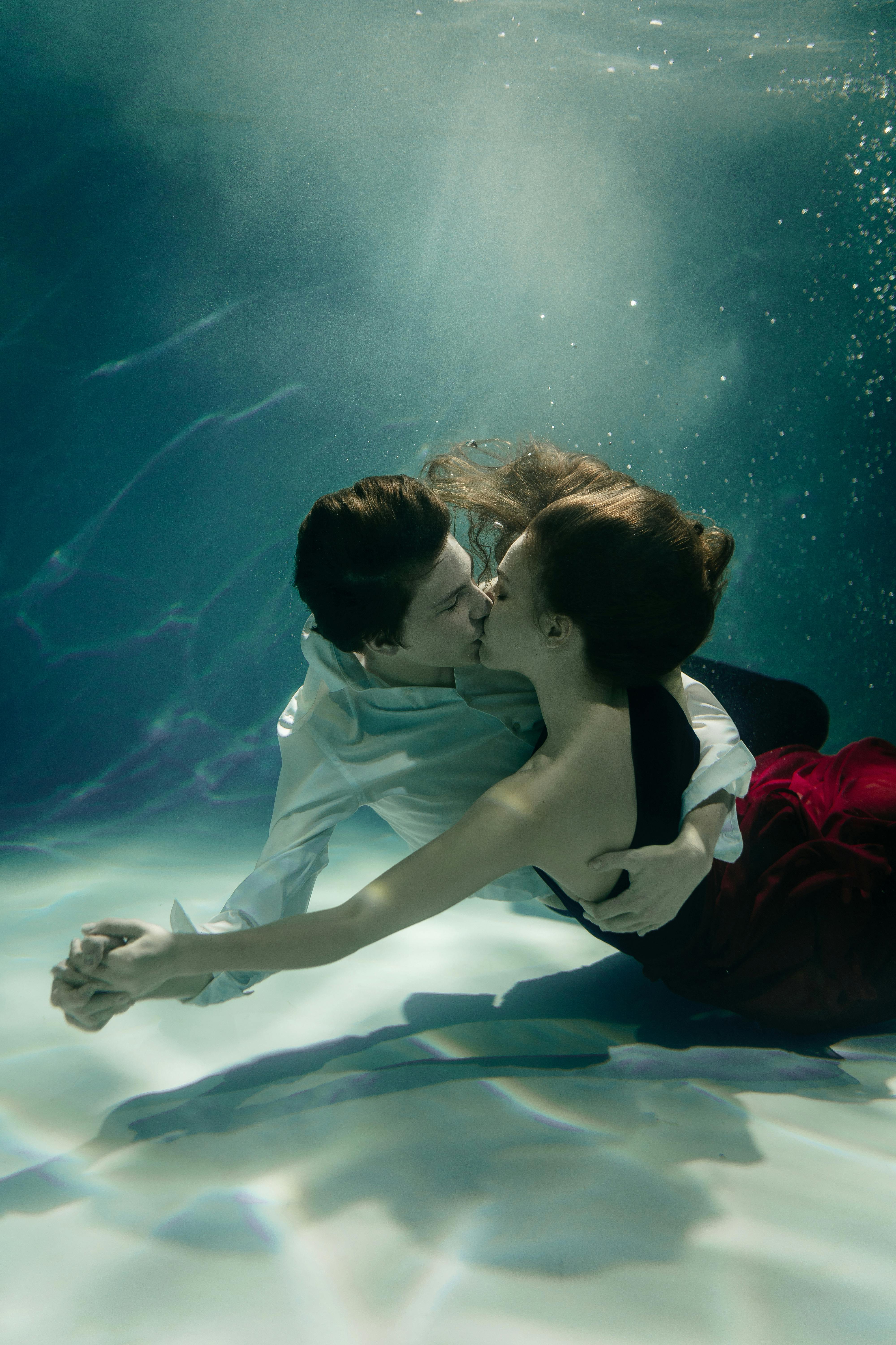 A couple delicately embraces and kisses underwater, capturing a sense of romance and surreal elegance.