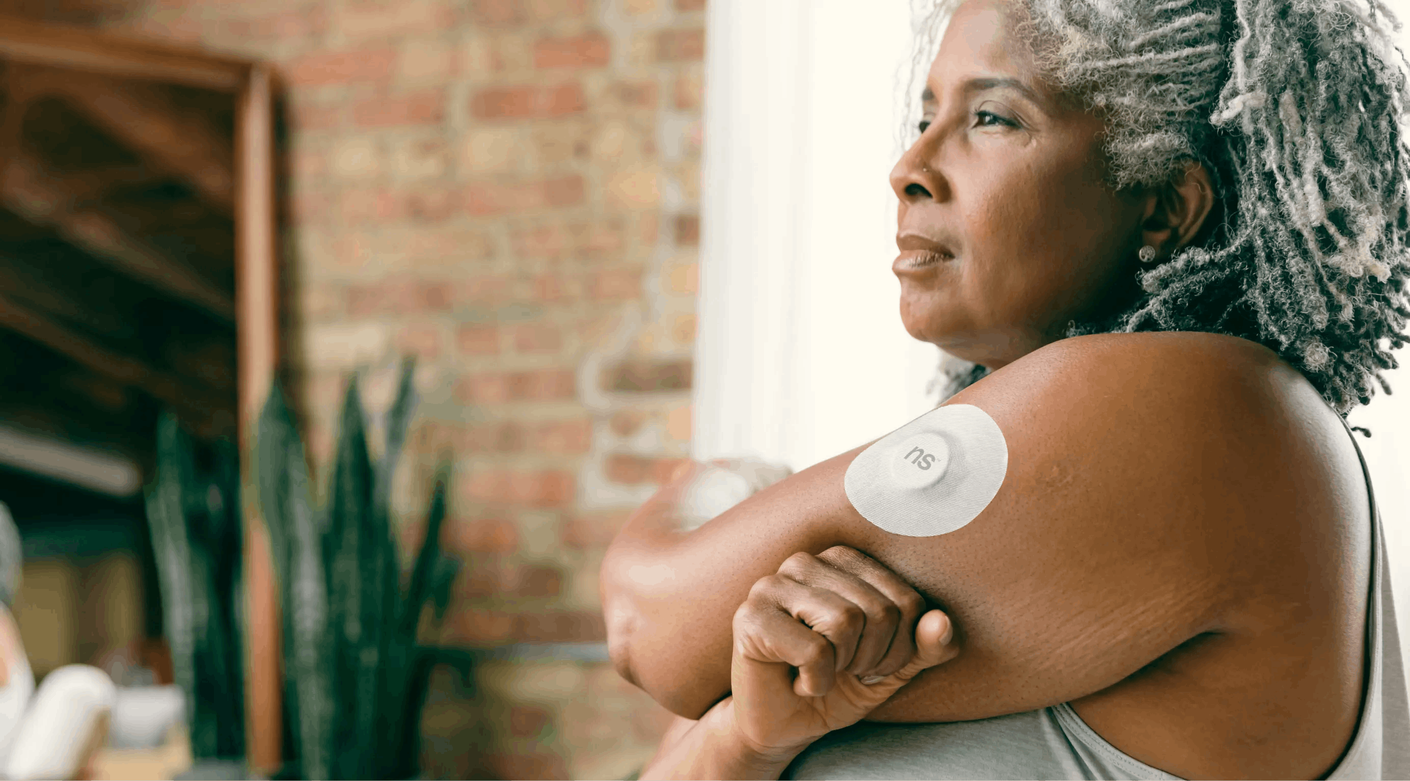 A mature woman with gray hair wearing a continuous glucose monitoring device on her arm.