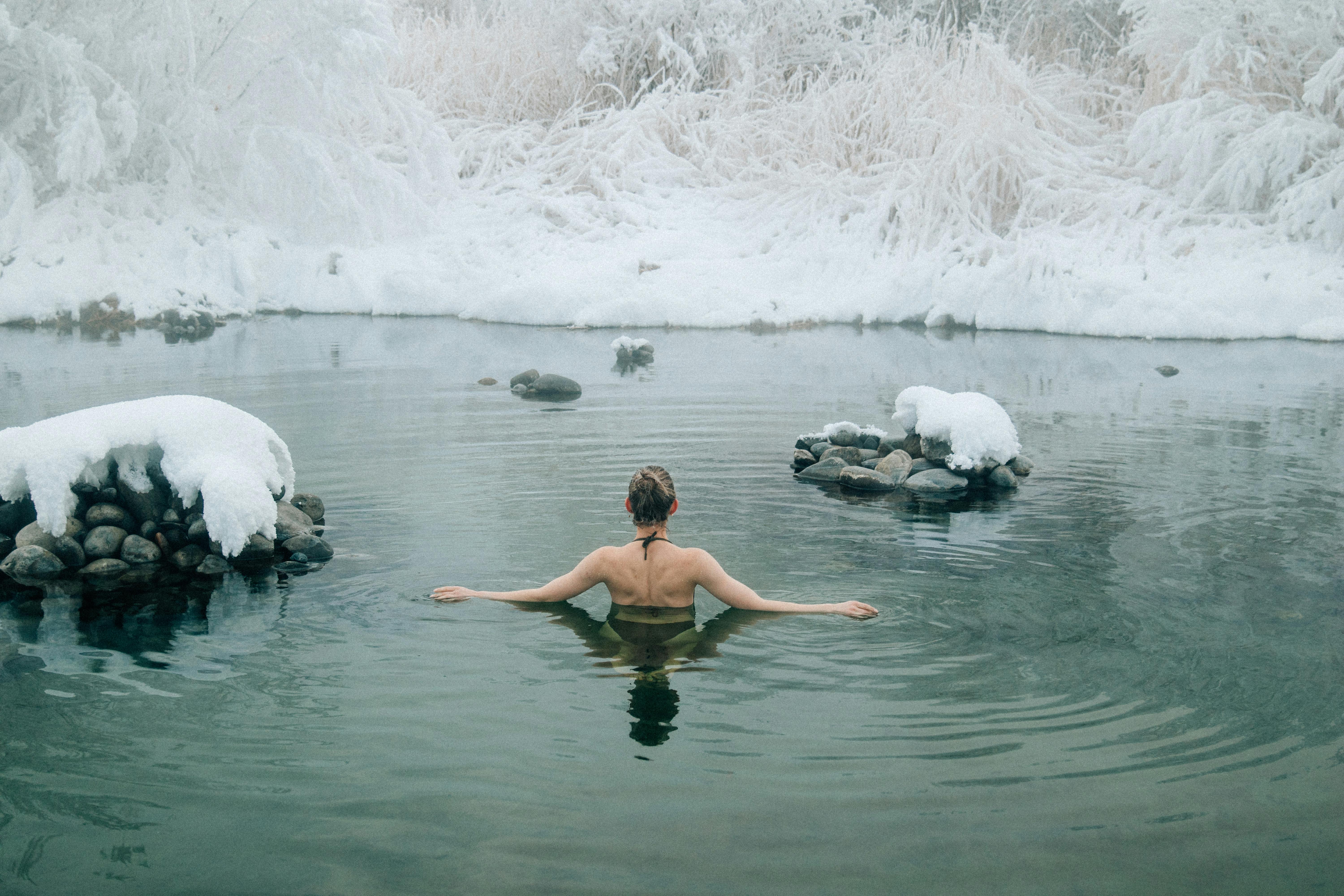 A young woman enjoying a swim in a tranquil winter lake surrounded by snow.