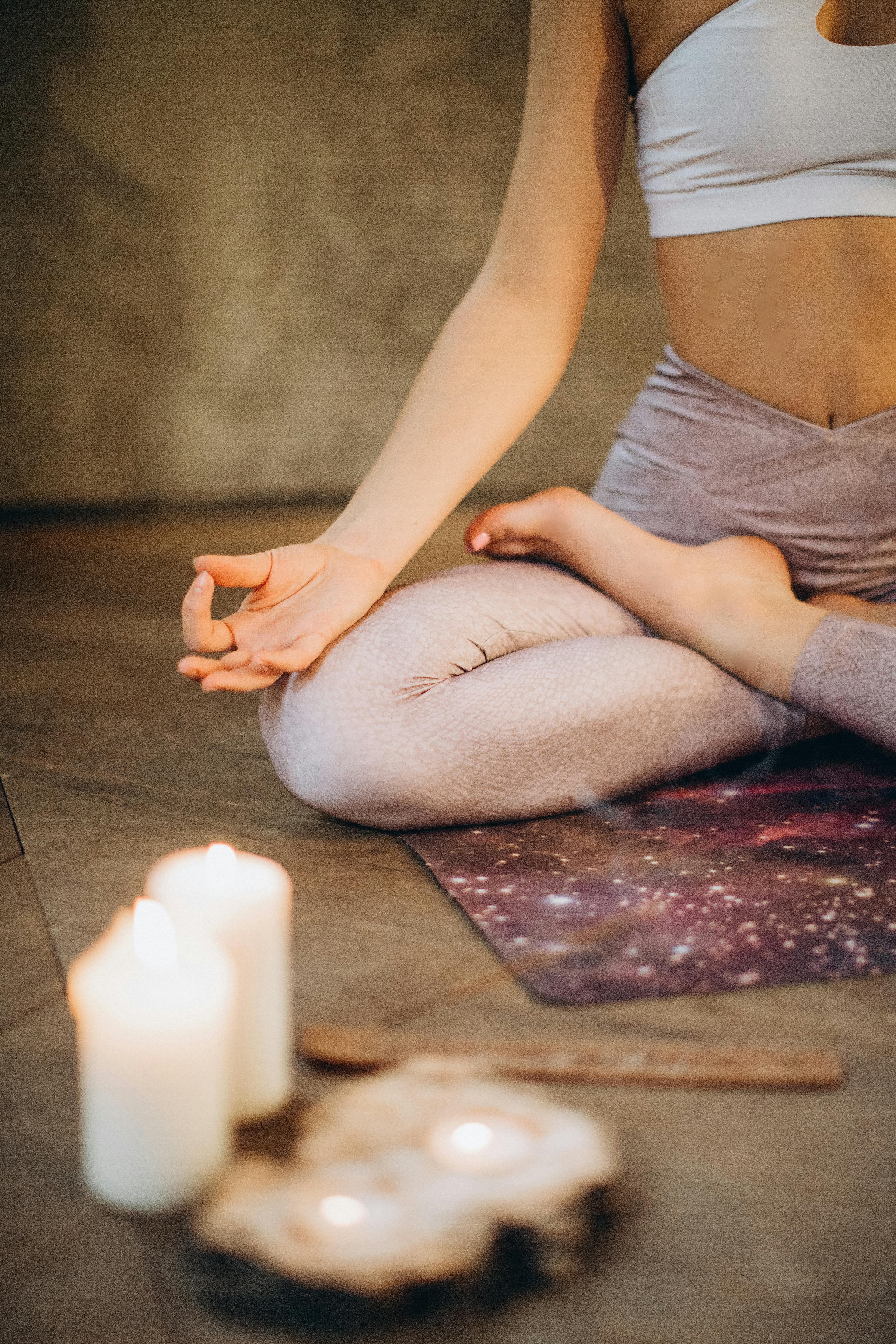 A woman practicing yoga indoors in lotus pose with candles creating a calming atmosphere.