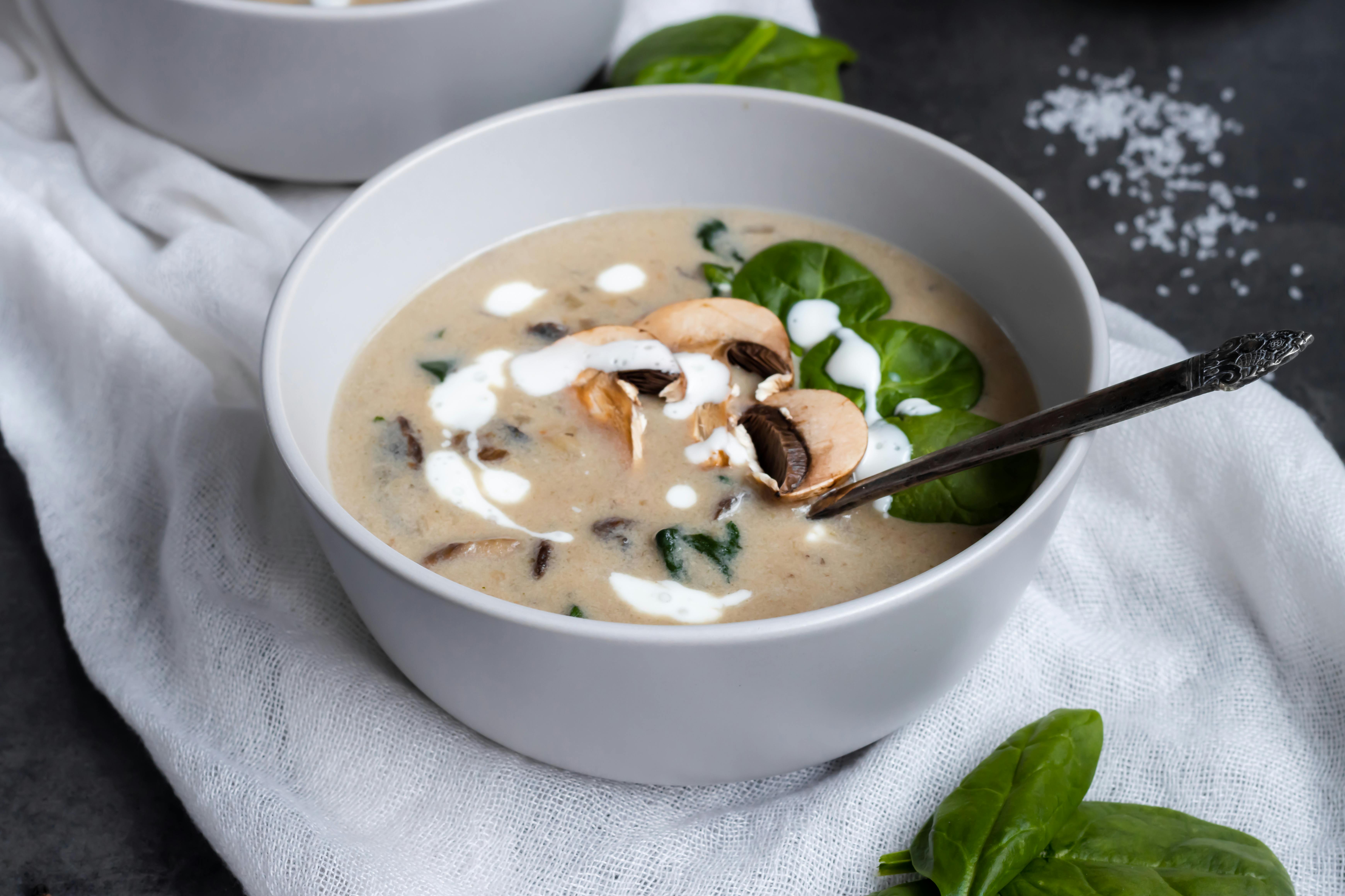 Delicious creamy mushroom soup garnished with fresh spinach leaves in a ceramic bowl.