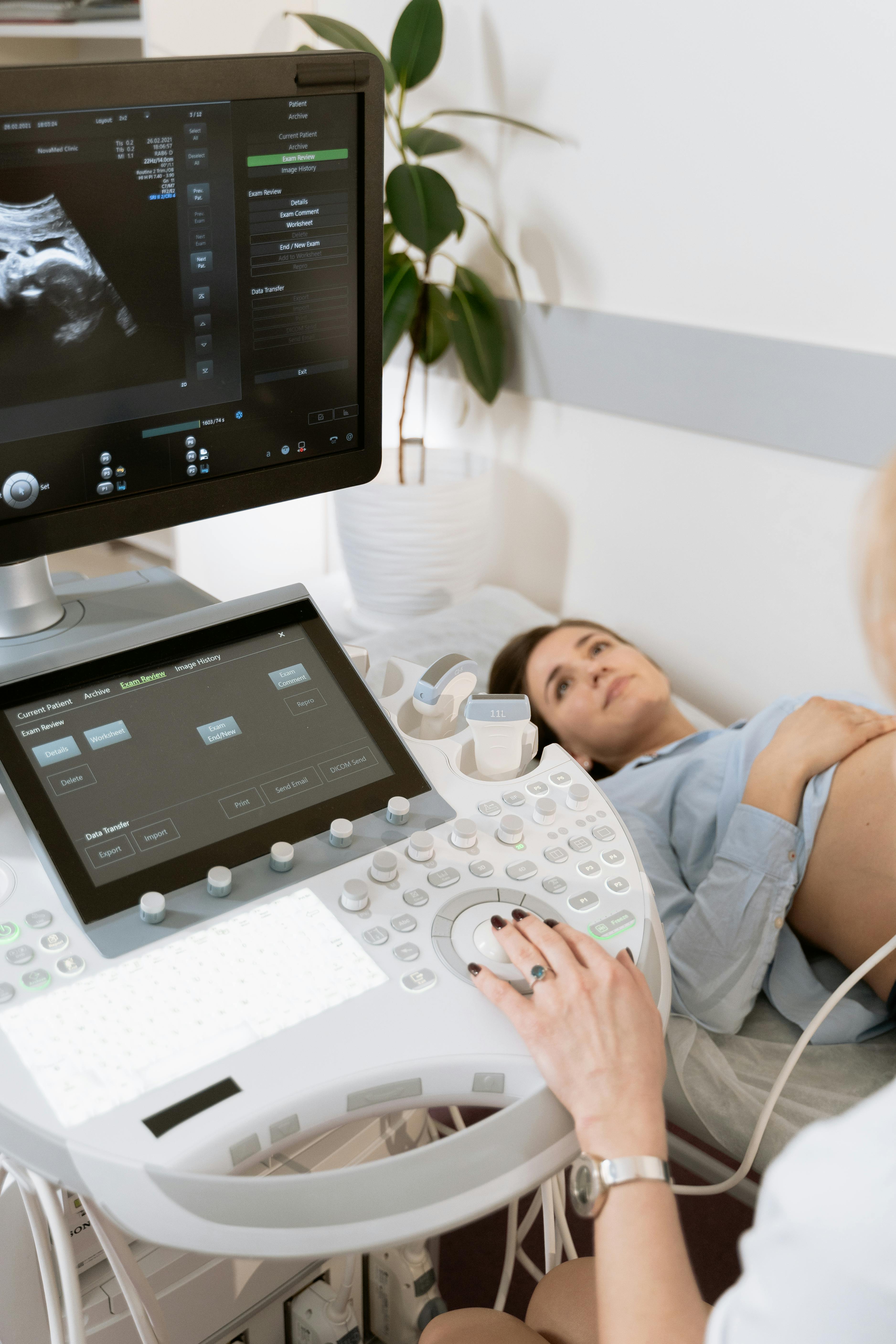 Pregnant woman undergoes ultrasound scan by medical professional in hospital room.