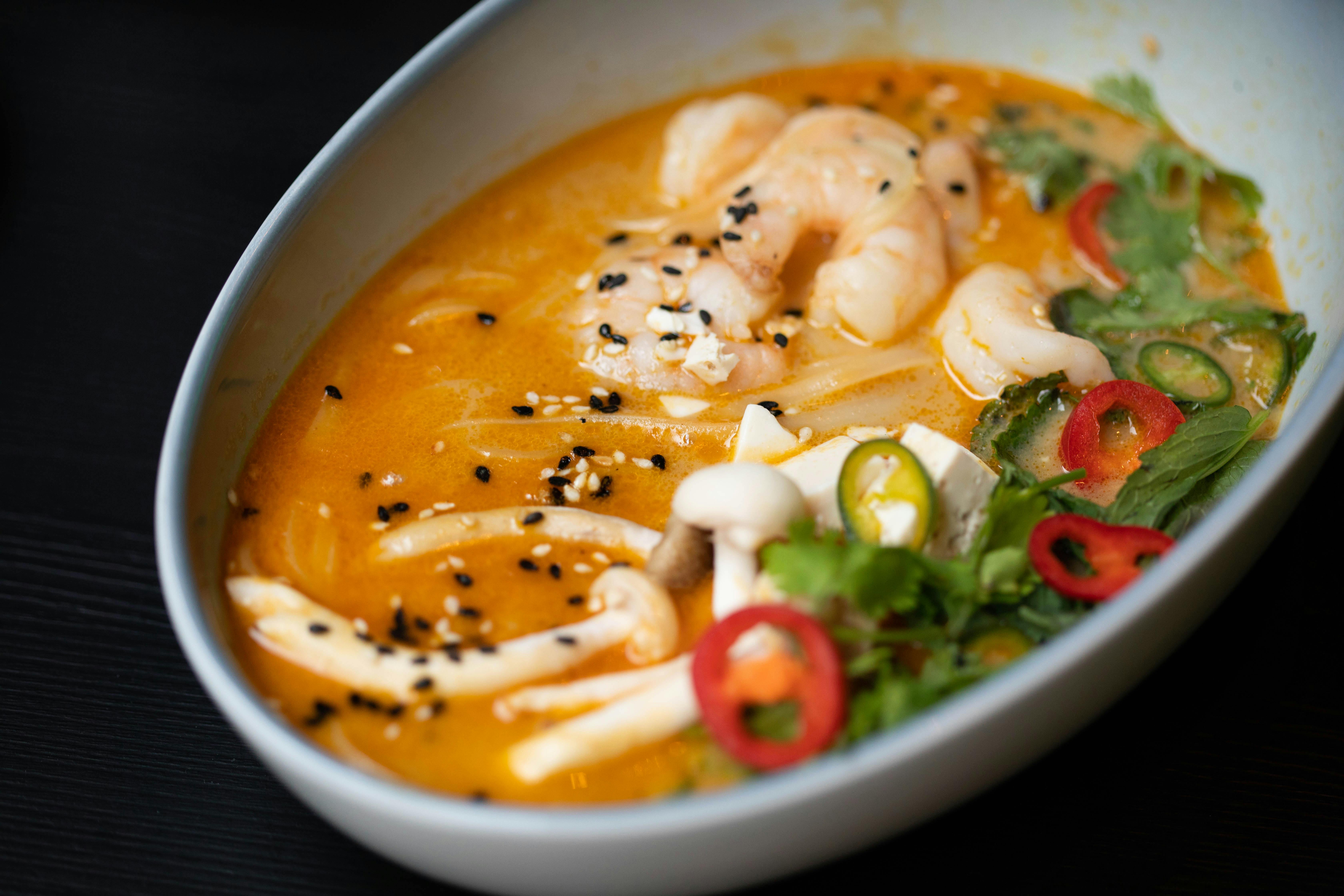 From above of delicious miso soup with funchosa shrimps and mushrooms served with tofu cheese and sliced vegetables decorated with chopped parsley and chili peppers