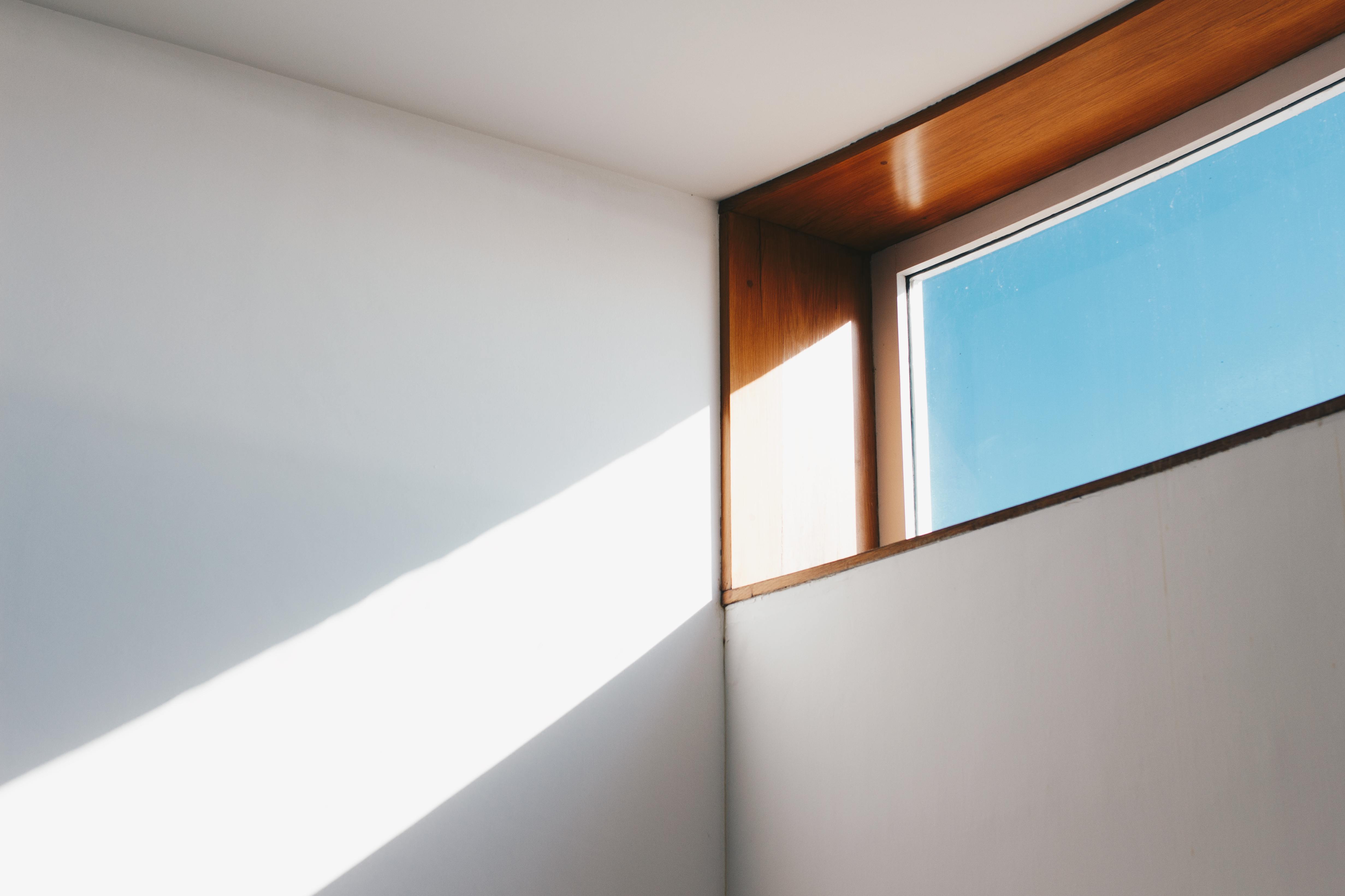 A minimalist interior showcasing sunlight streaming through a modern glass window against a blue sky.