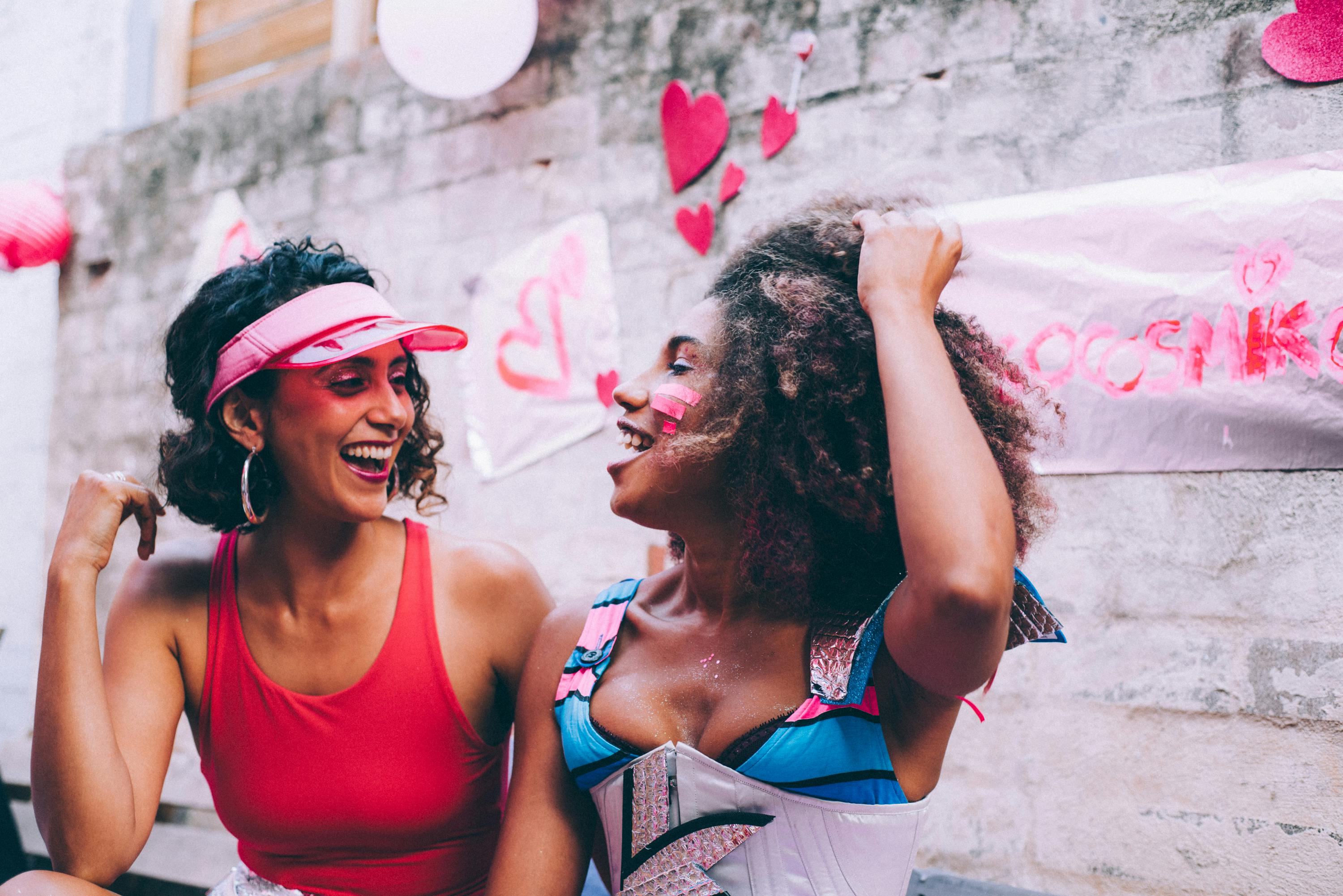 Two women laughing together at a colorful outdoor celebration with heart decorations.