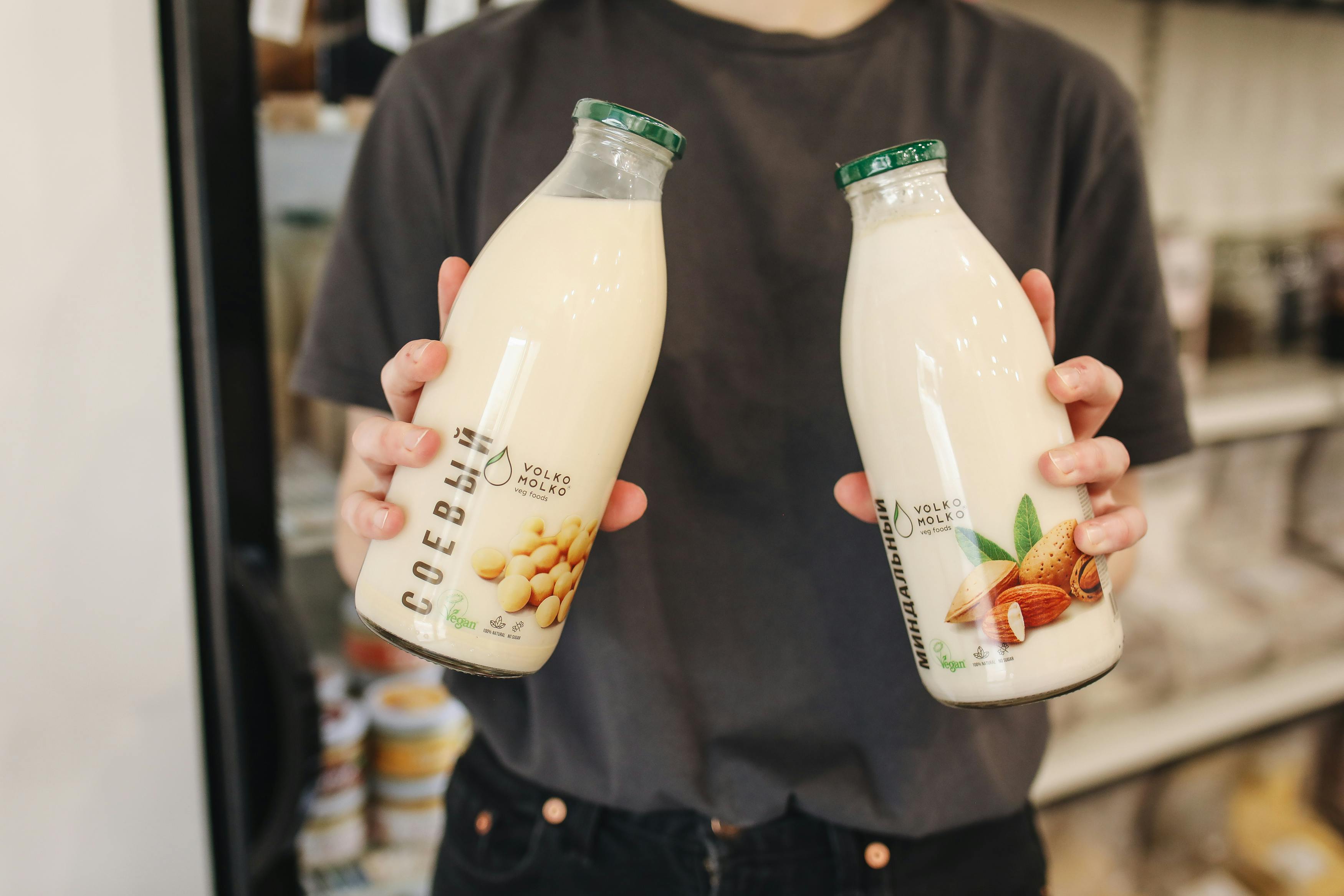 Person holding bottles of almond and soy milk substitutes in a store.