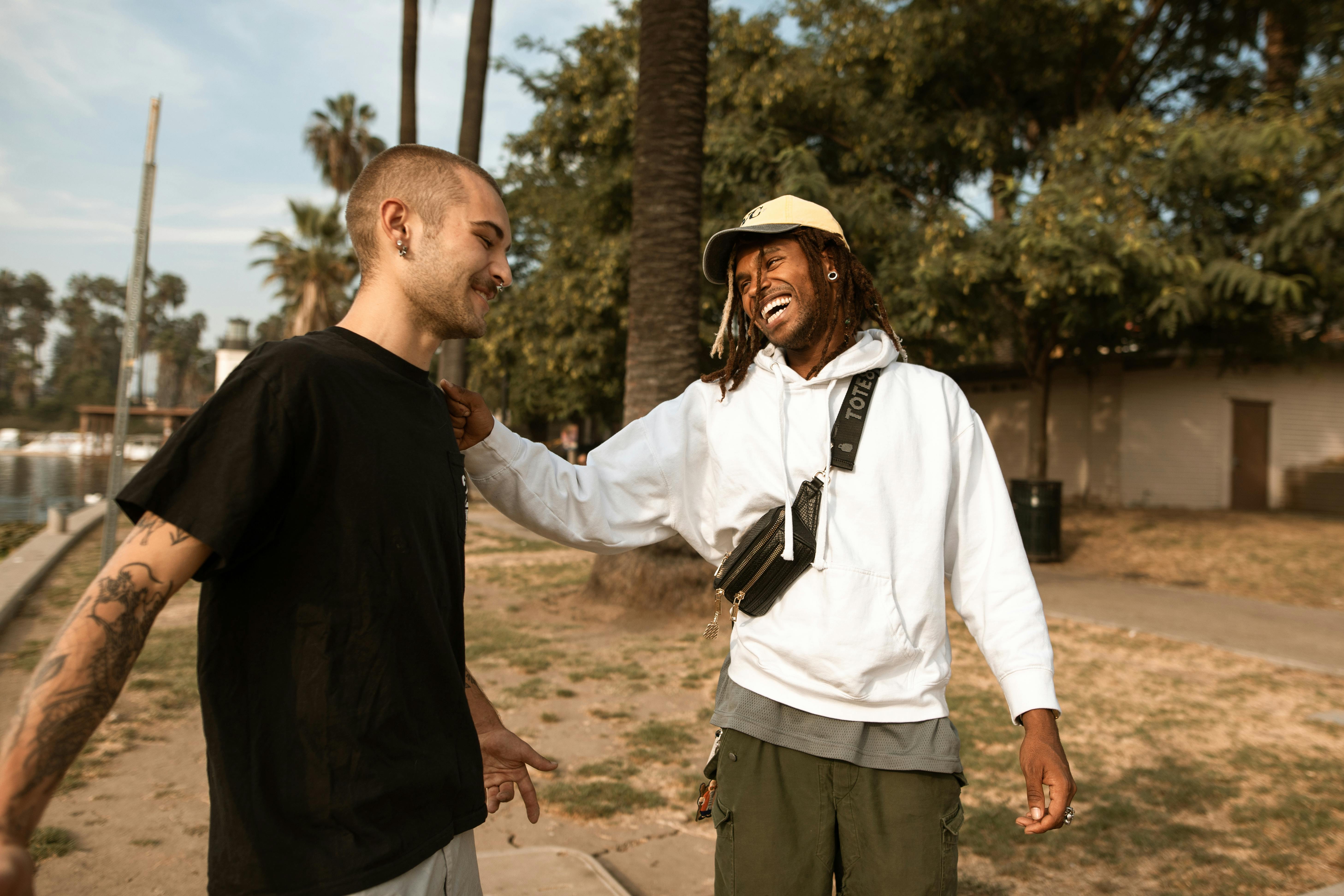 Two friends laughing and bonding outdoors in a sunny park, showcasing friendship and leisure.