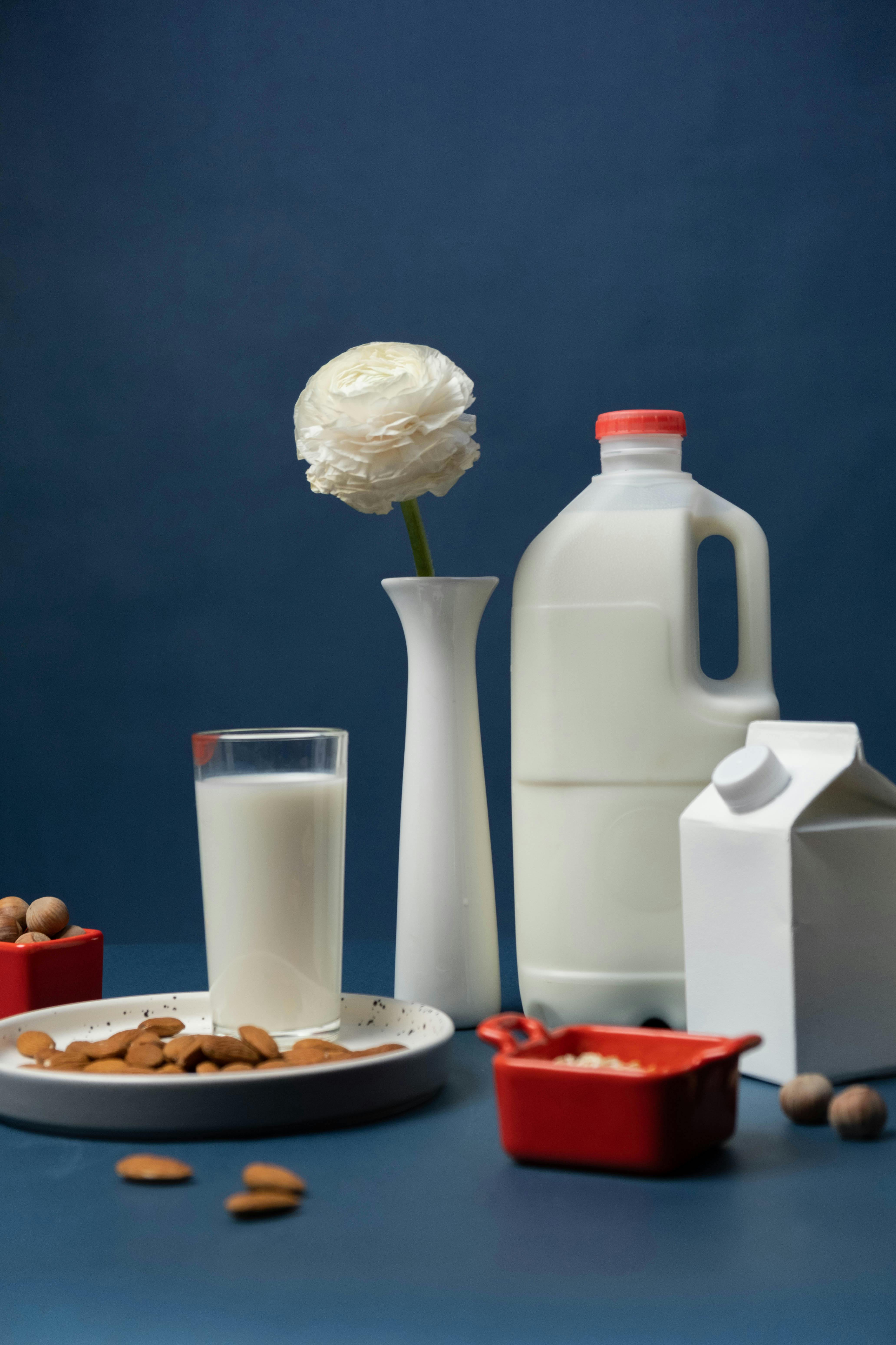 A creative arrangement of almond milk, nuts, and white rose with blue backdrop.